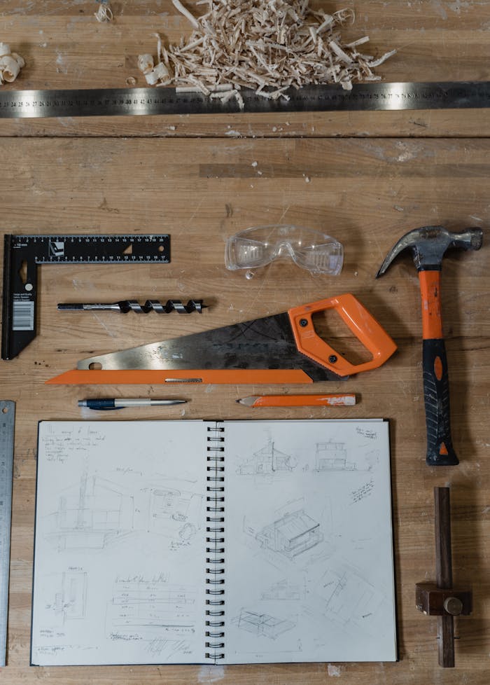 Flatlay of carpentry tools and a sketch notebook on a wood workbench.